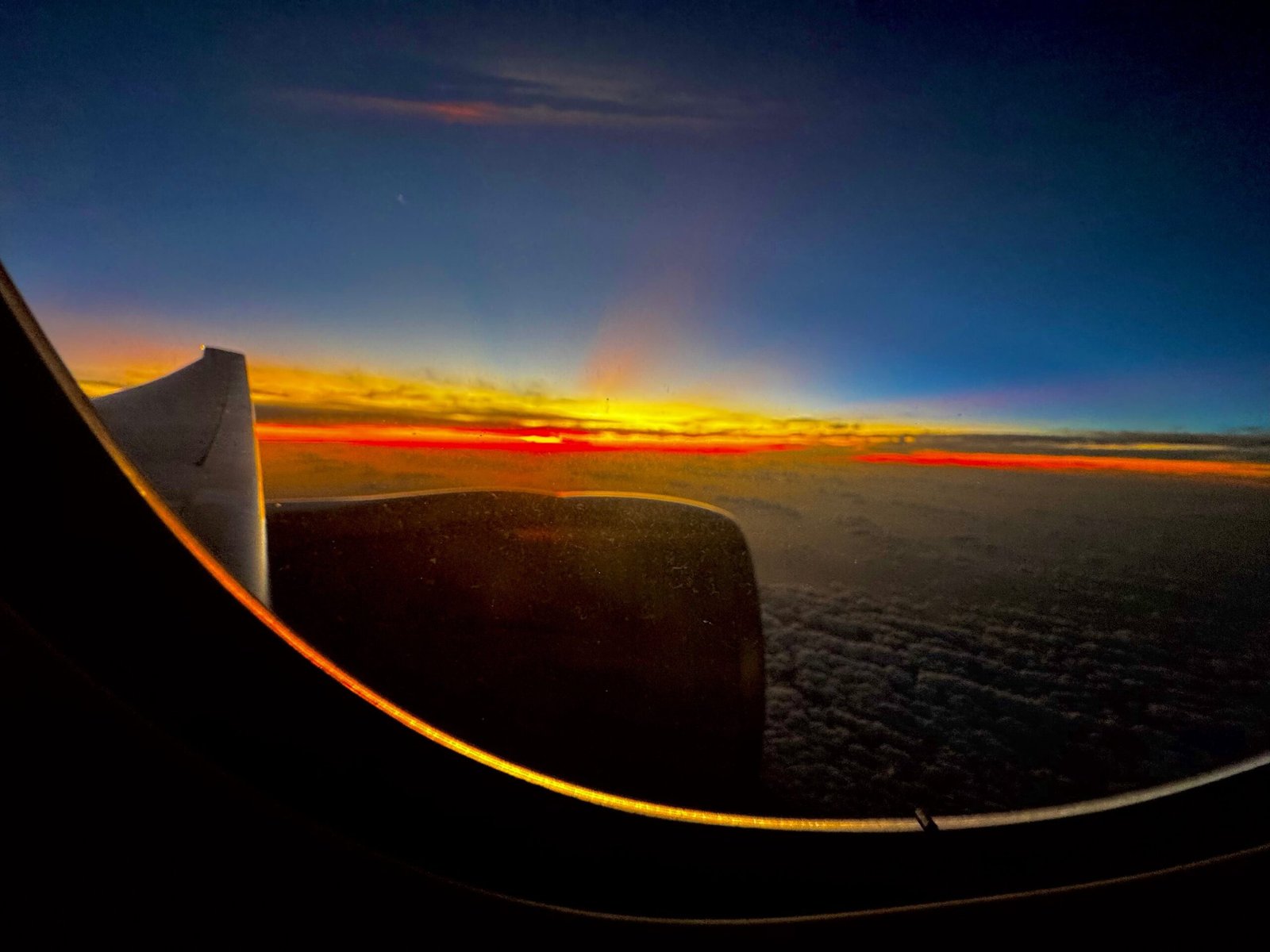 View from an airplane window of a fiery sunrise above the clouds