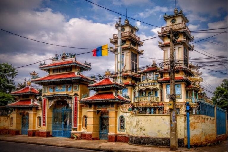 Ornate gate of a Cao Dai temple with twin towers and a colorful flag