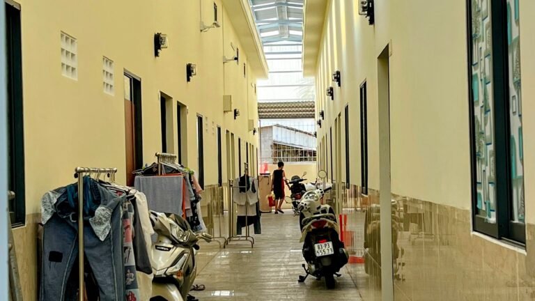Covered walkway lined with parked motorbikes and drying laundry outside rented rooms in provincial Vietnam