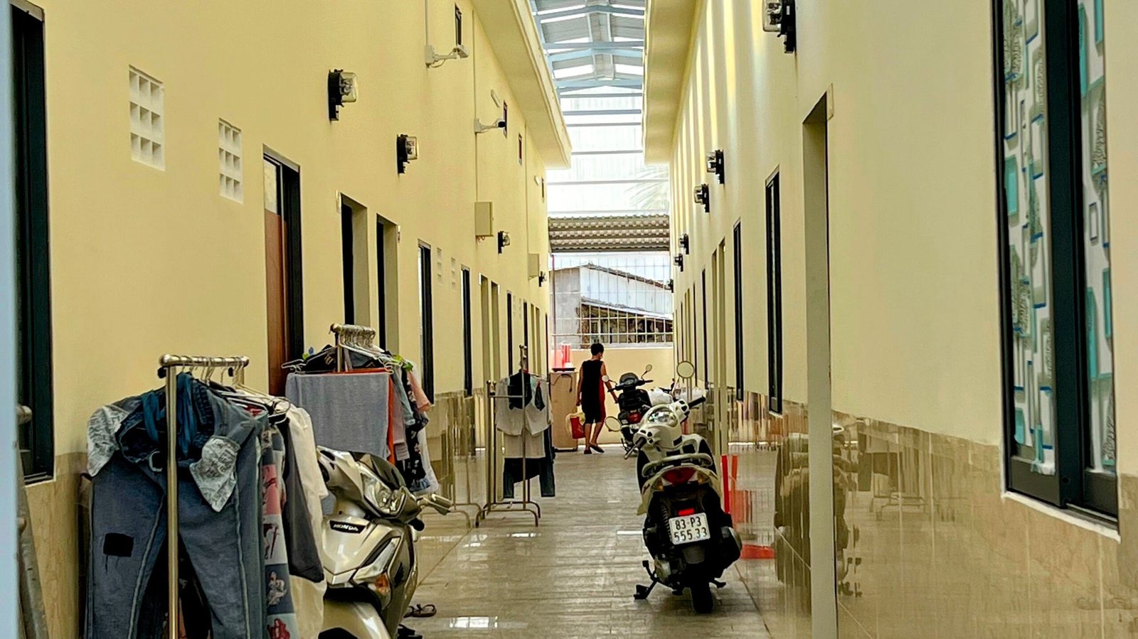 Covered walkway lined with parked motorbikes and drying laundry outside rented rooms in provincial Vietnam