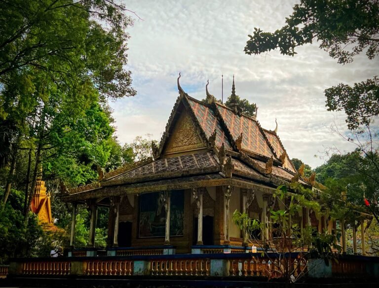 Khmer-style Buddhist temple with an ornate carved gable roof, surrounded by trees