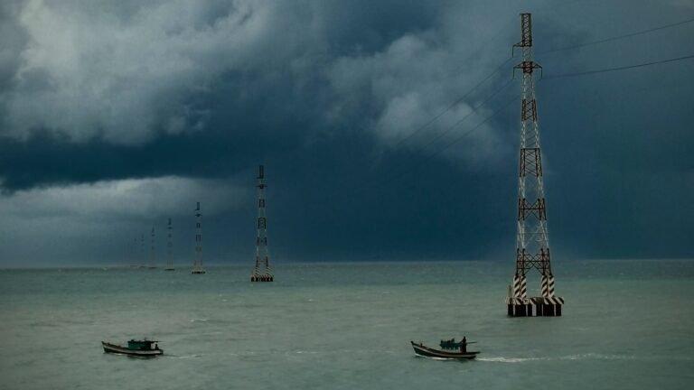 Power line pylons crossing the sea toward Hon Son Island under storm clouds, with small fishing boats passing