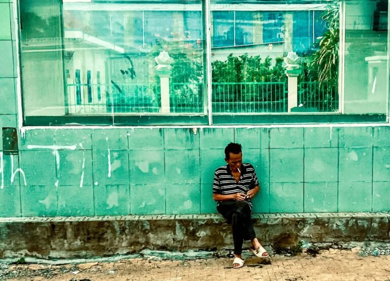 Man sitting and smoking against a weathered green tiled wall in Vietnam