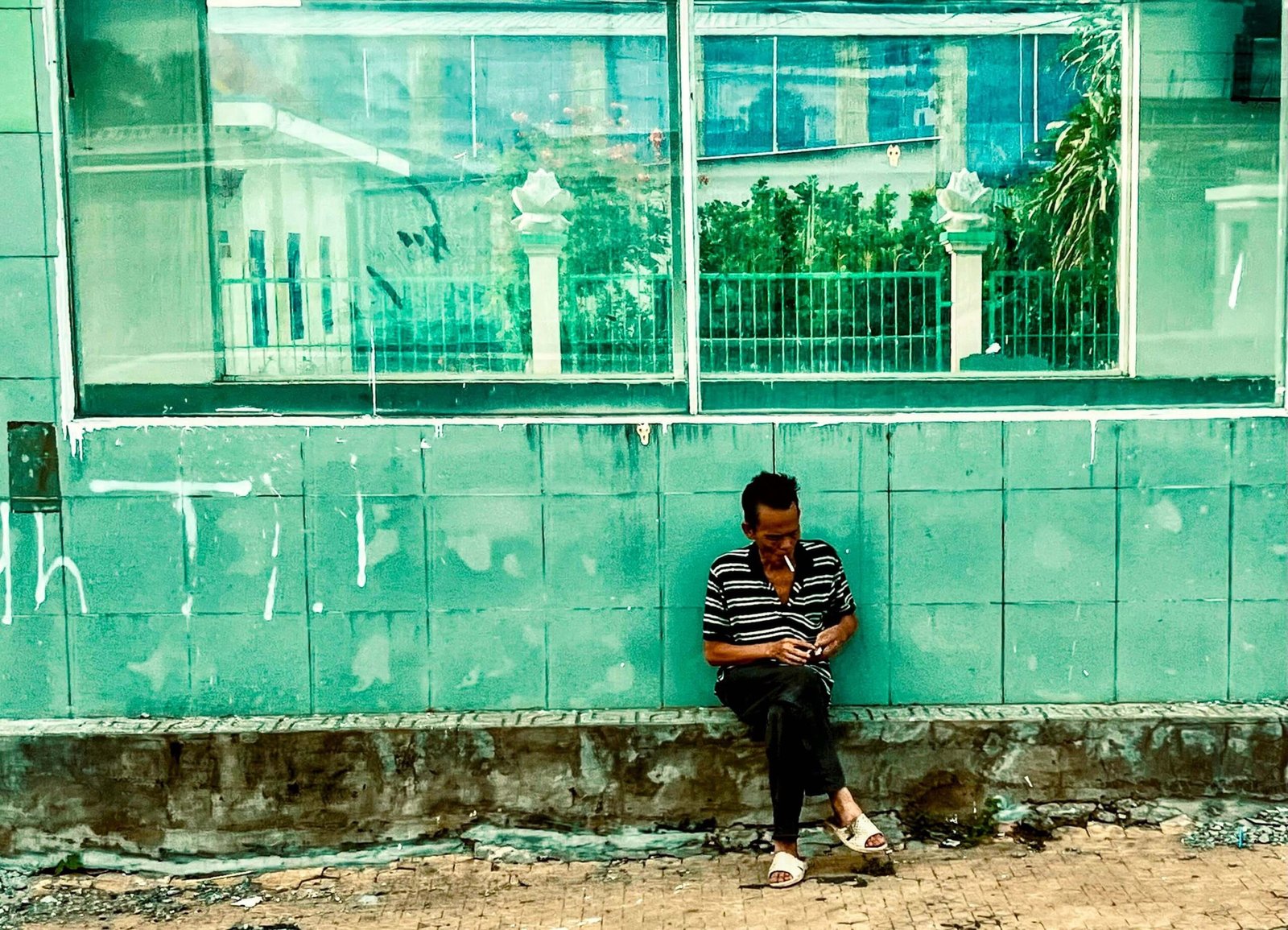 Man sitting and smoking against a weathered green tiled wall in Vietnam