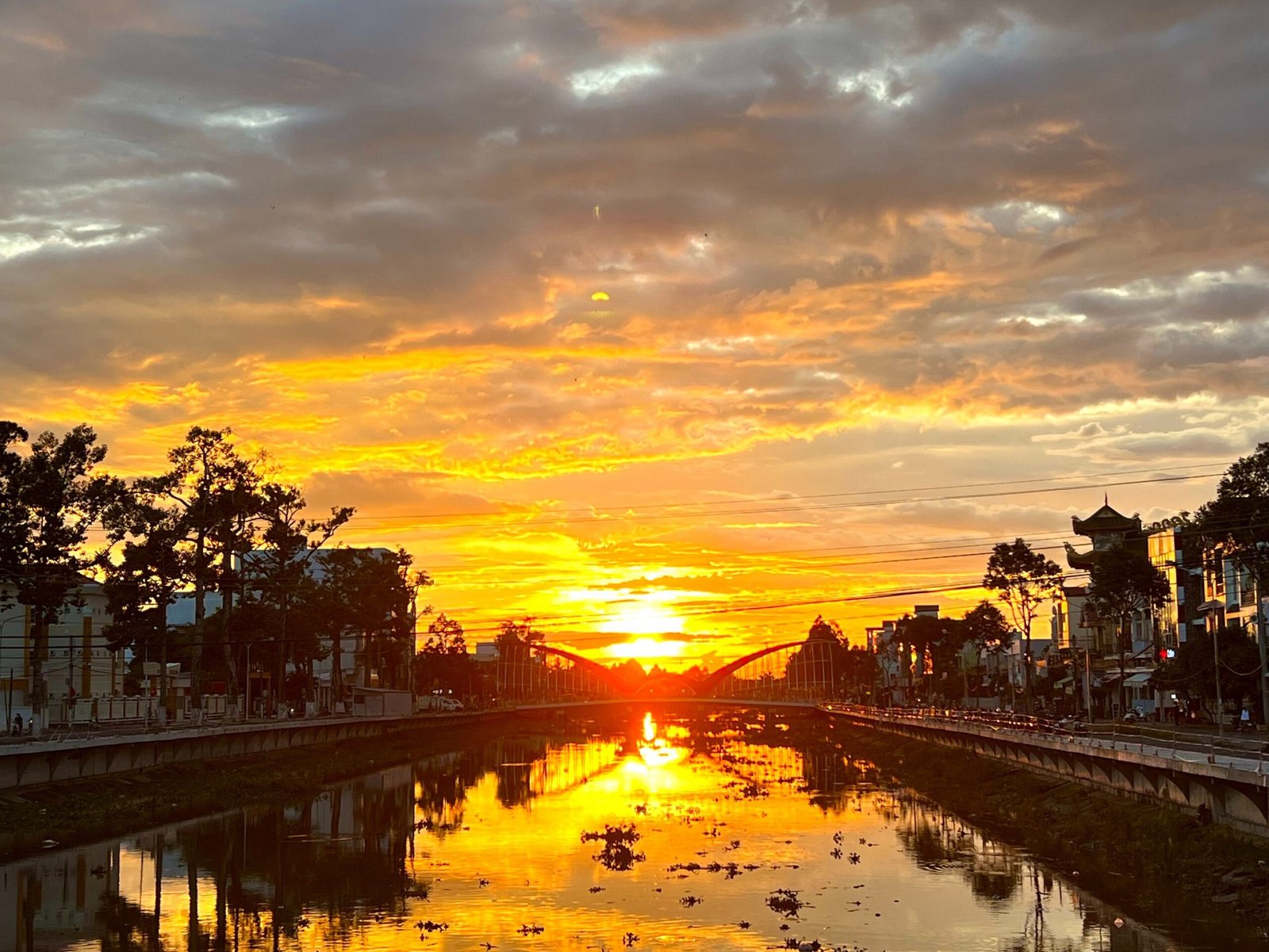 Fiery sunset over the Maspero River in Soc Trang City, with a bridge silhouette reflected in the water