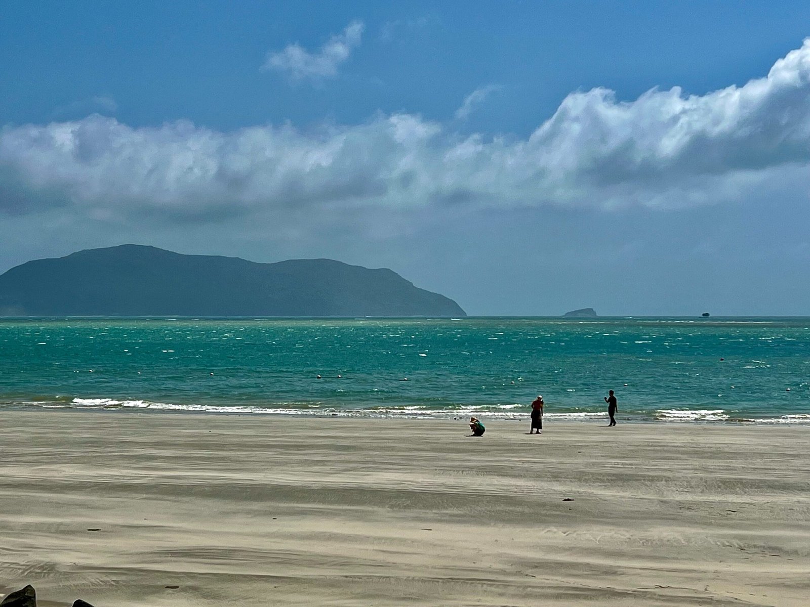 Quiet Con Dao beach with two people walking, mountains in the distance