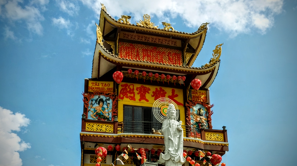 Multi-tiered pagoda facade with a white Quan Am statue and red lanterns