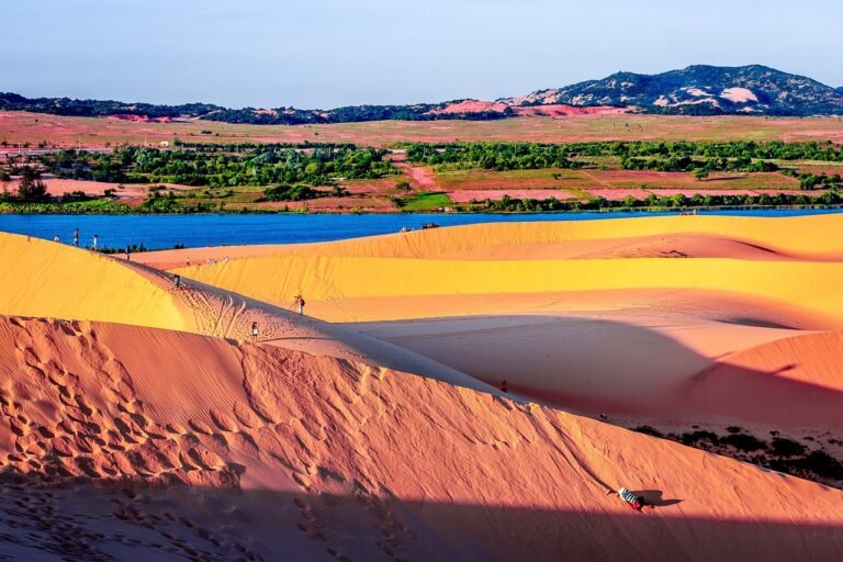 Red and gold sand dunes at Mui Ne with a lake and green fields in the distance