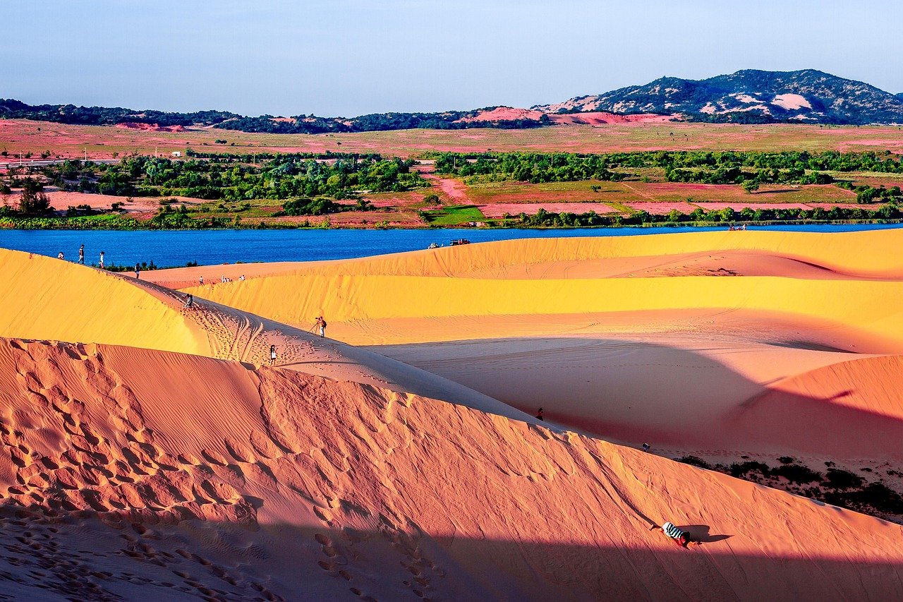 Red and gold sand dunes at Mui Ne with a lake and green fields in the distance