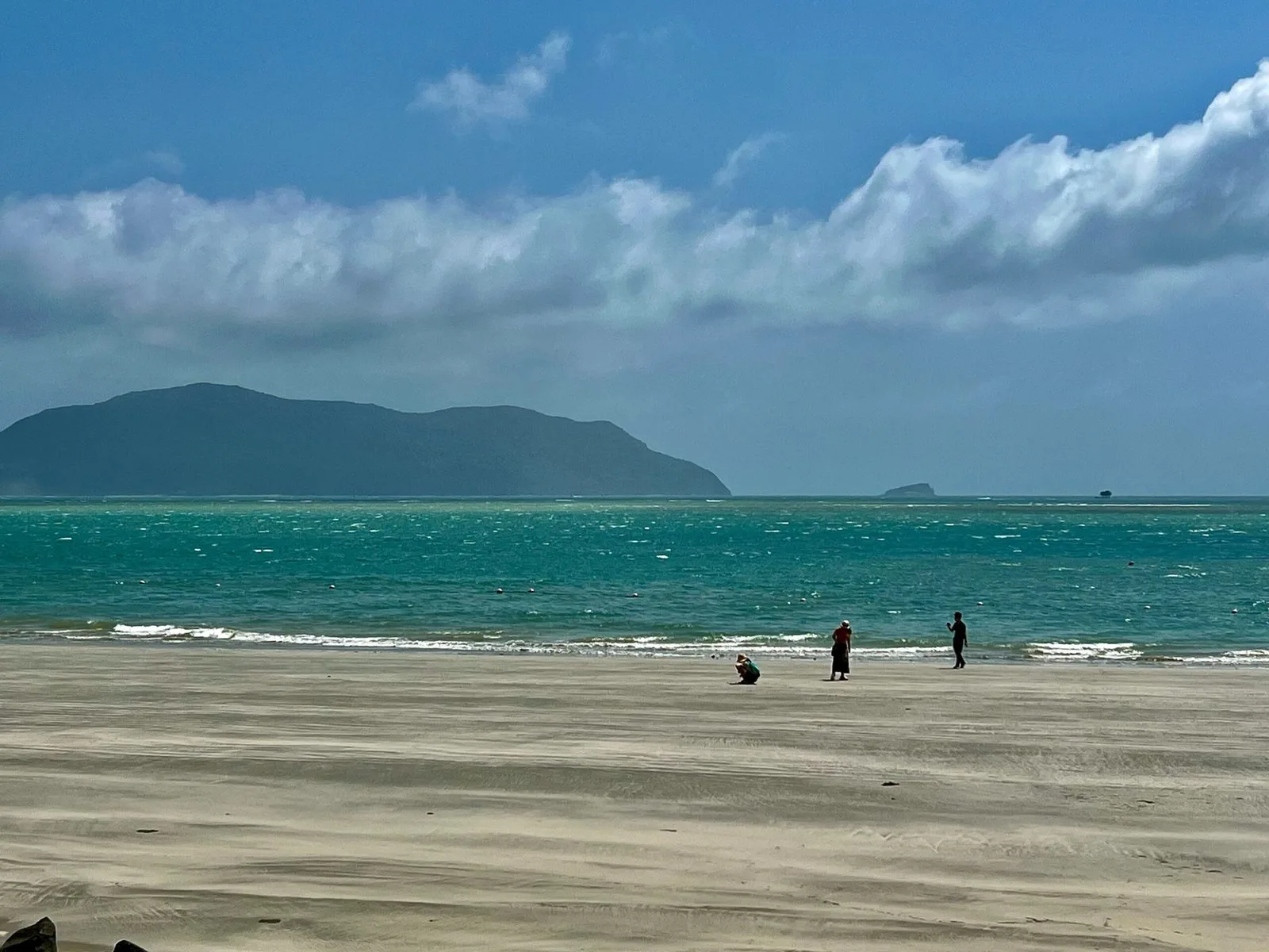 Quiet Con Dao beach with two people walking, mountains in the distance