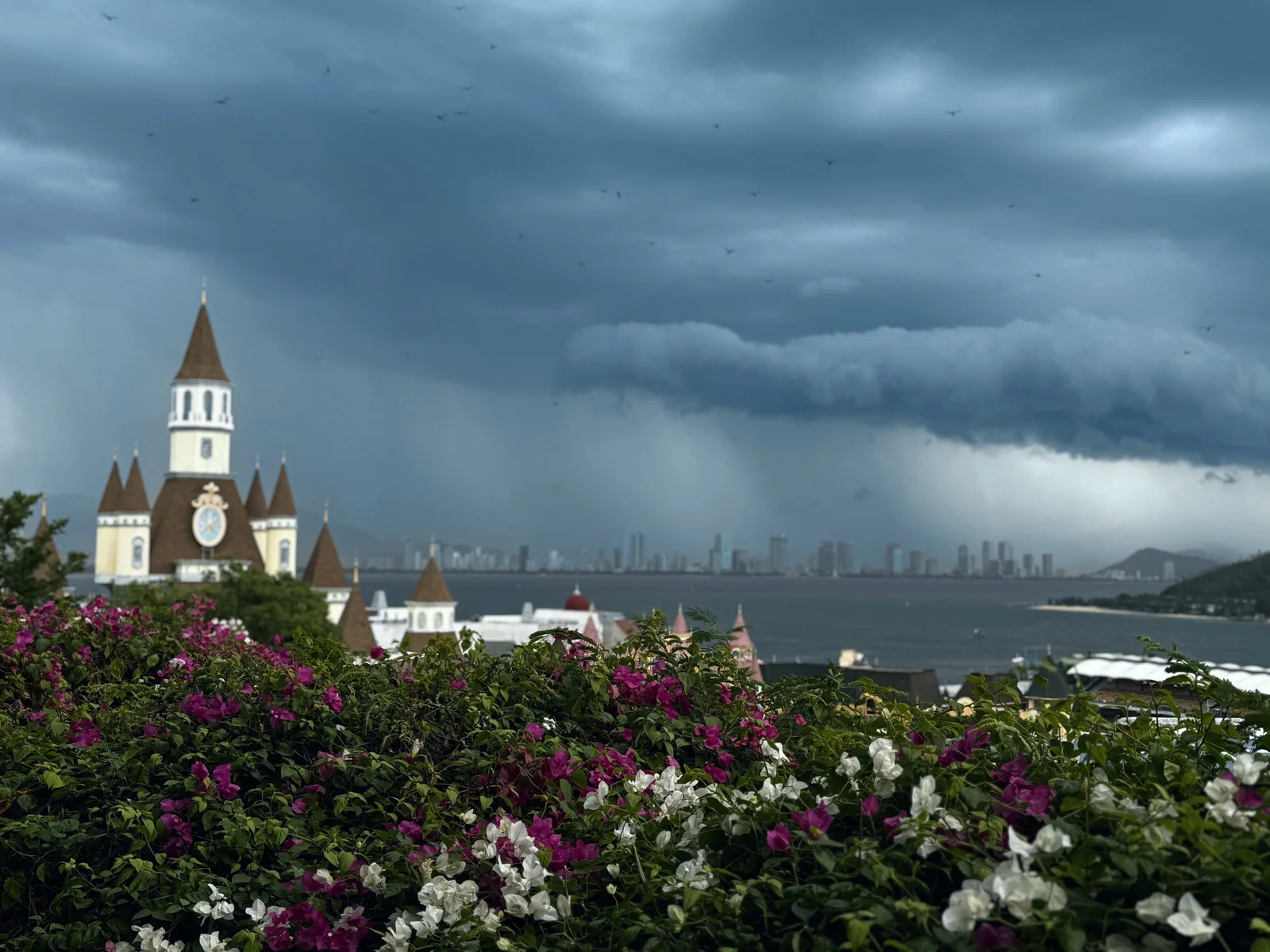 Storm clouds rolling over Nha Trang bay in July, seen from VinWonders, with bougainvillea in the foreground