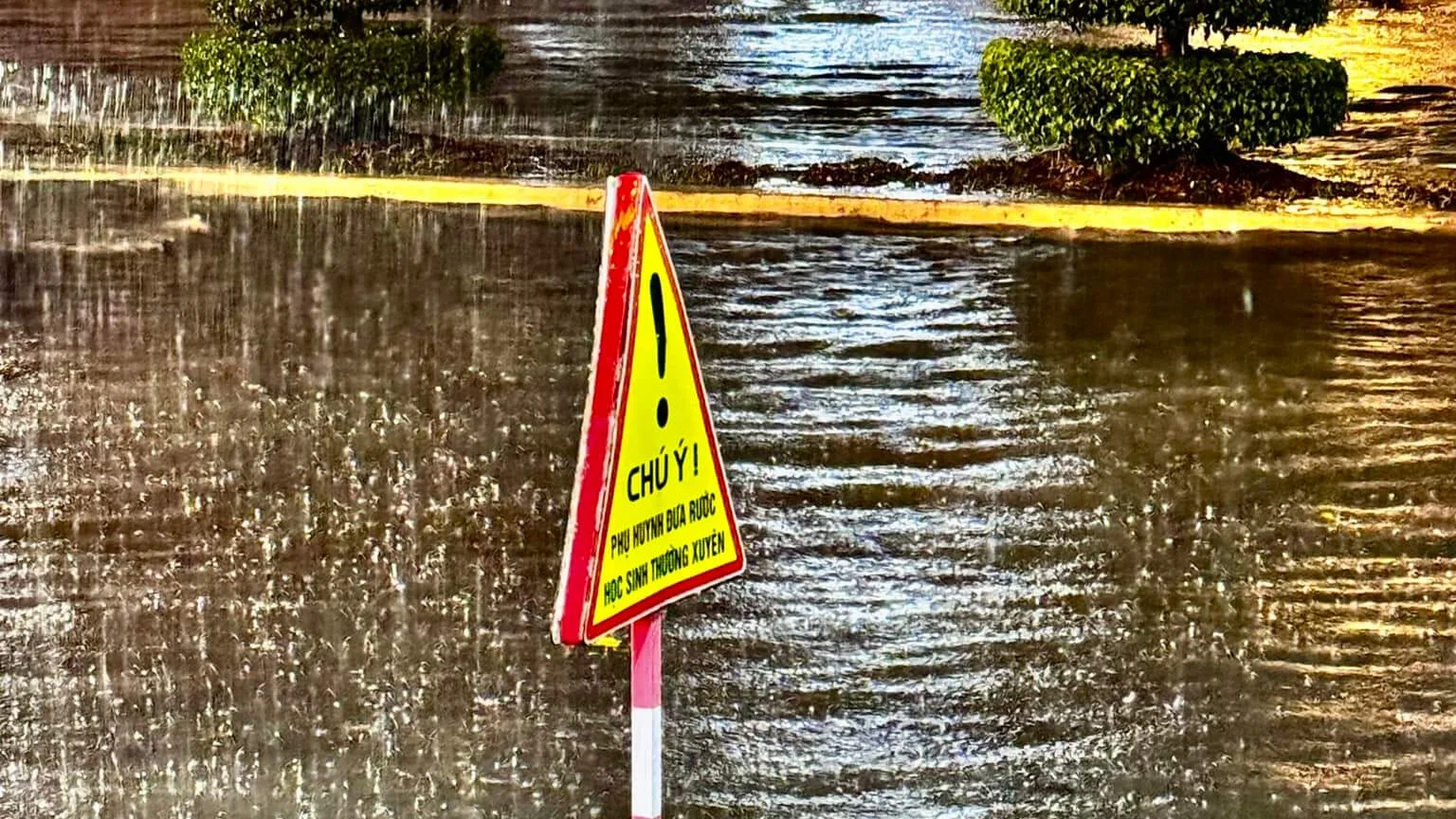 Flooded street in Sóc Trăng at night during the rainy season, with a school-zone warning sign standing in the water